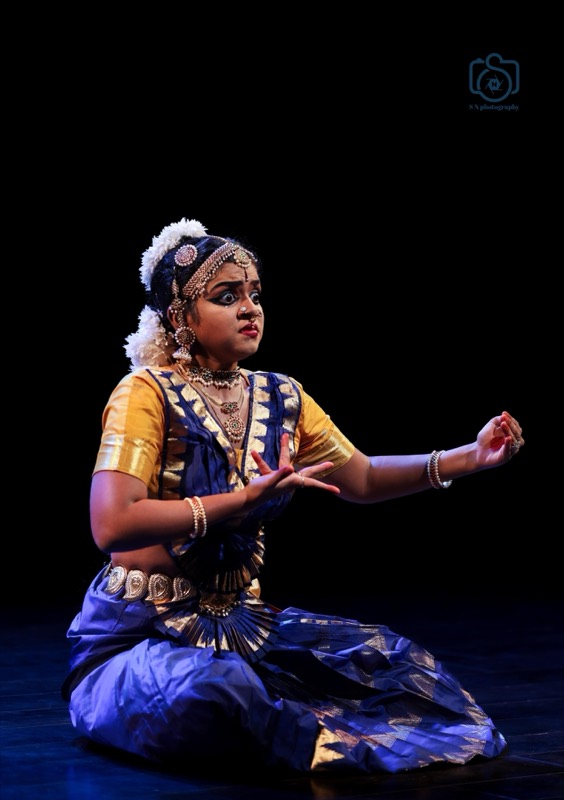 Dancer seated in blue and gold, mid-expression