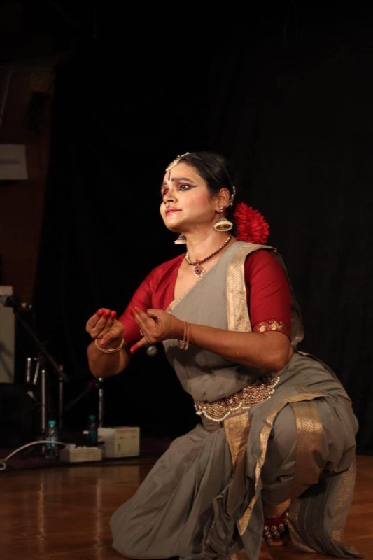 Teacher in a grey and red costume, kneeling mid-dance